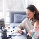 Eine Mutter arbeitet mit ihrem Baby am Schreibtisch und zeigt, wie sich Homeoffice mit Baby einrichten lässt.