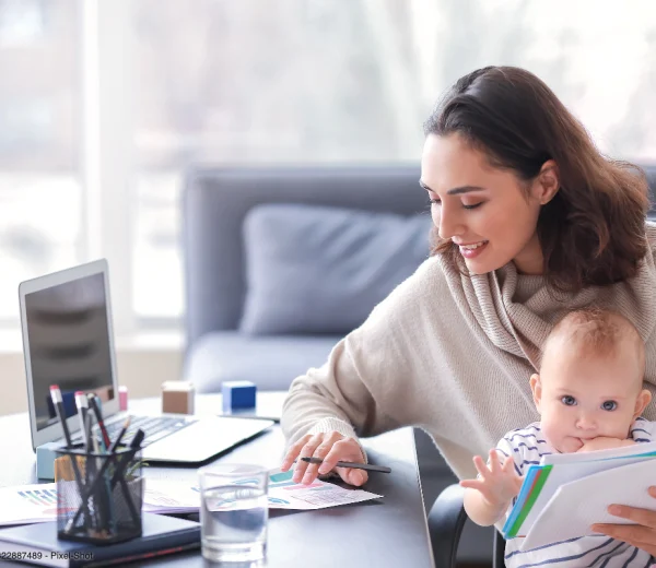 Eine Mutter arbeitet mit ihrem Baby am Schreibtisch und zeigt, wie sich Homeoffice mit Baby einrichten lässt.